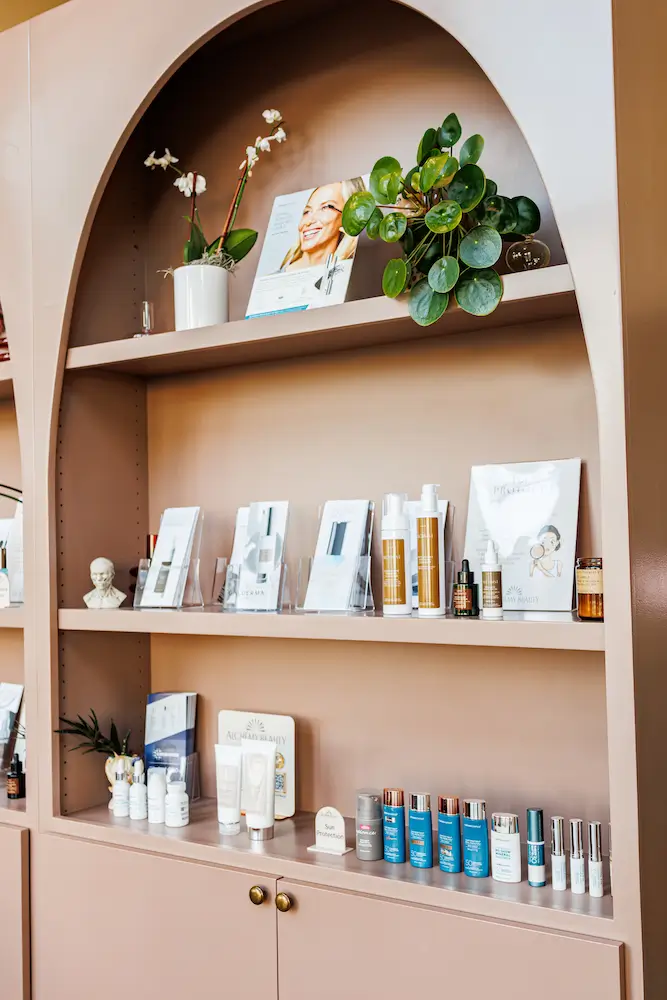 A decorative shelving unit with skincare products, plants, and promotional materials. The design features an arched top and pastel color scheme.