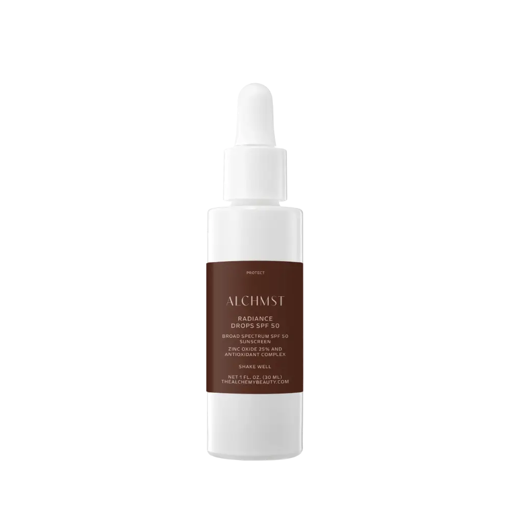 White bottle with dropper, labeled "ALCHMST Radiance Drops SPF 50," featuring zinc oxide and antioxidant complex. Contains 1 fl. oz. by The Alchemy Beauty.