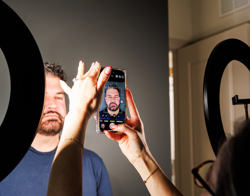 A smartphone capturing a person's portrait with ring lights. Another person holds the phone, positioning the shot for optimal lighting and focus.